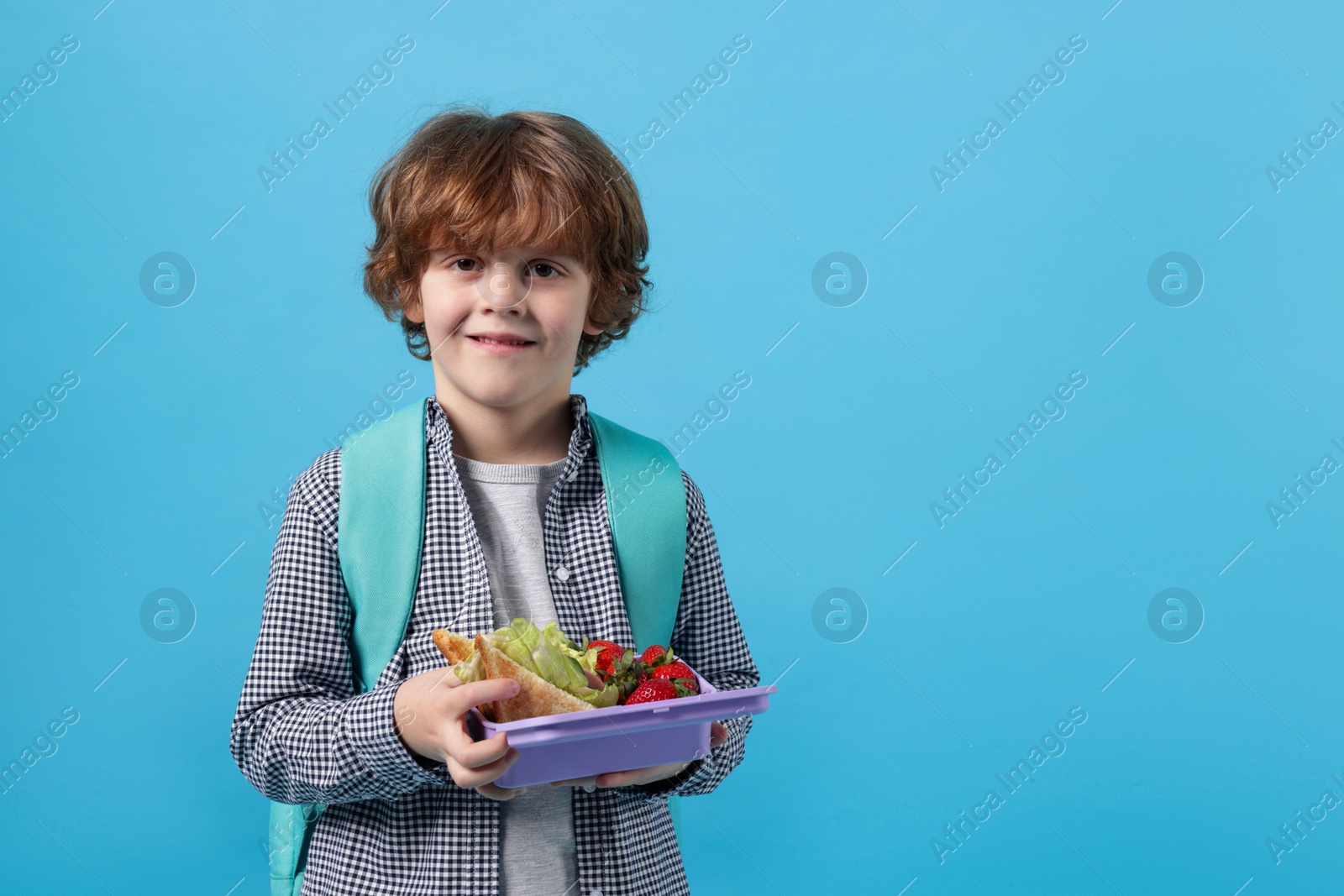 Photo of Cute little boy with lunch box on light blue background. Space for text