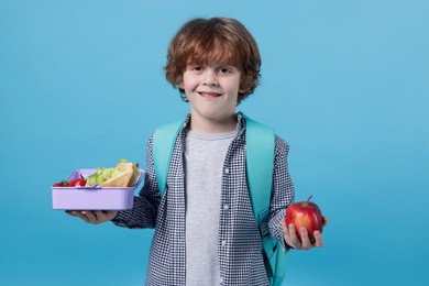 Photo of Cute little boy with lunch box and apple on light blue background