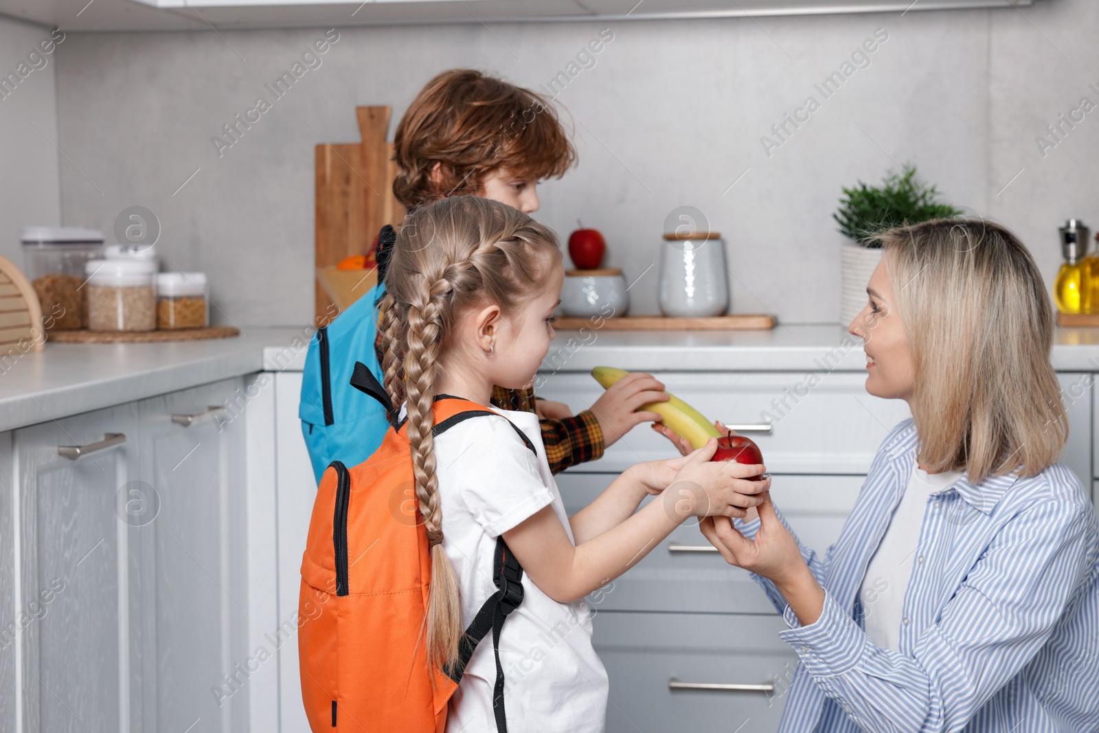 Photo of Mother giving her children fruits for school snacks in kitchen