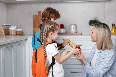 Mother giving her children fruits for school snacks in kitchen