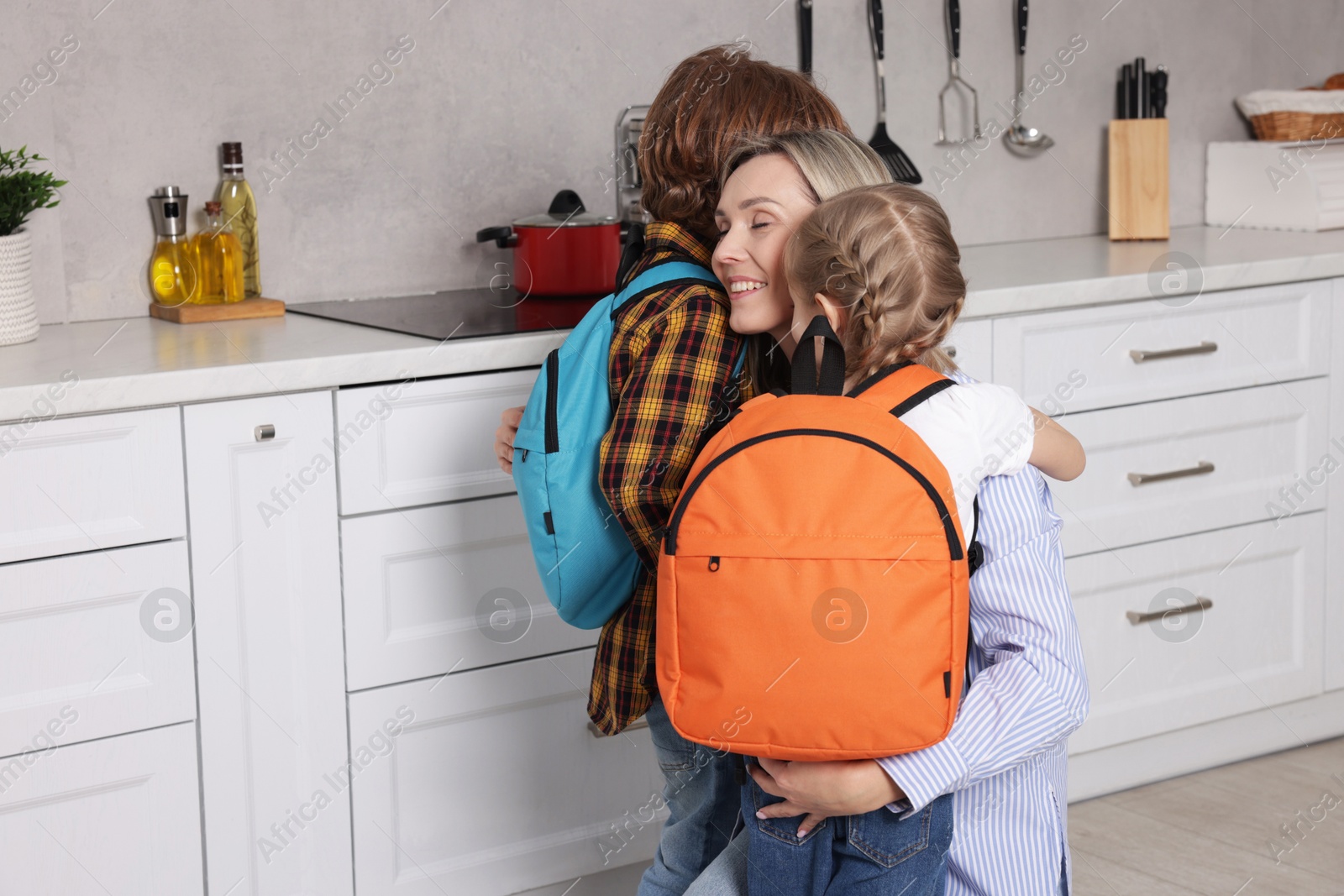 Photo of Mother and her cute children with backpacks hugging at home