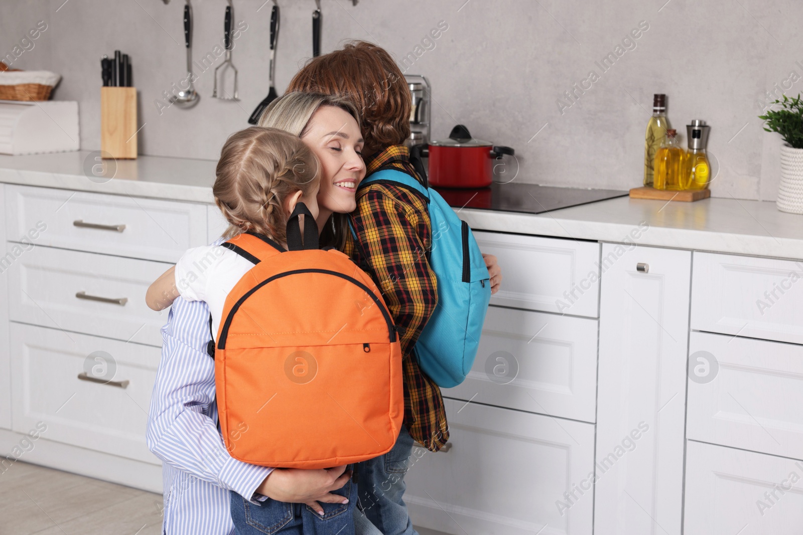 Photo of Mother and her cute children with backpacks hugging at home