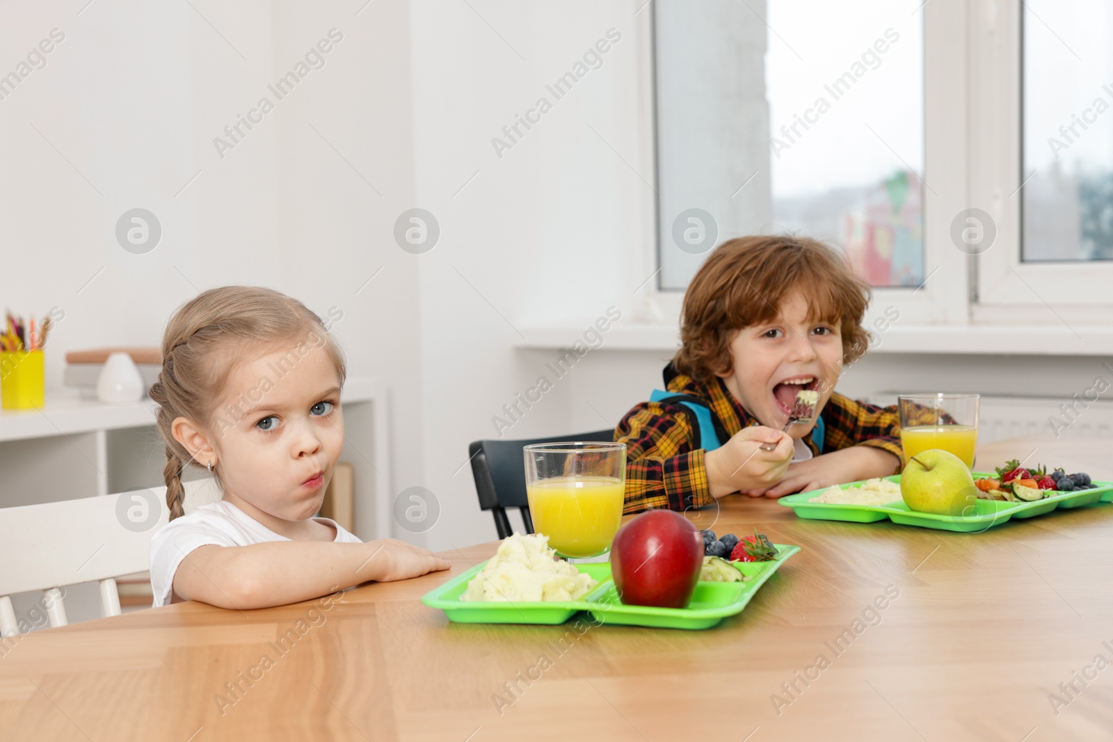 Photo of Cute little children eating lunch at wooden table in school