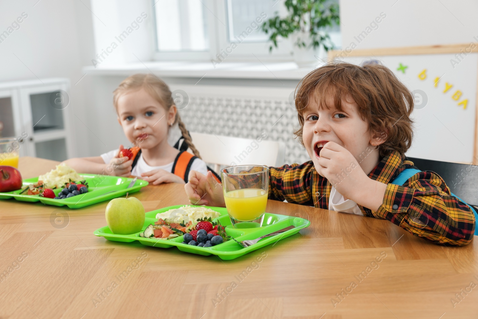 Photo of Cute little children eating lunch at wooden table in school