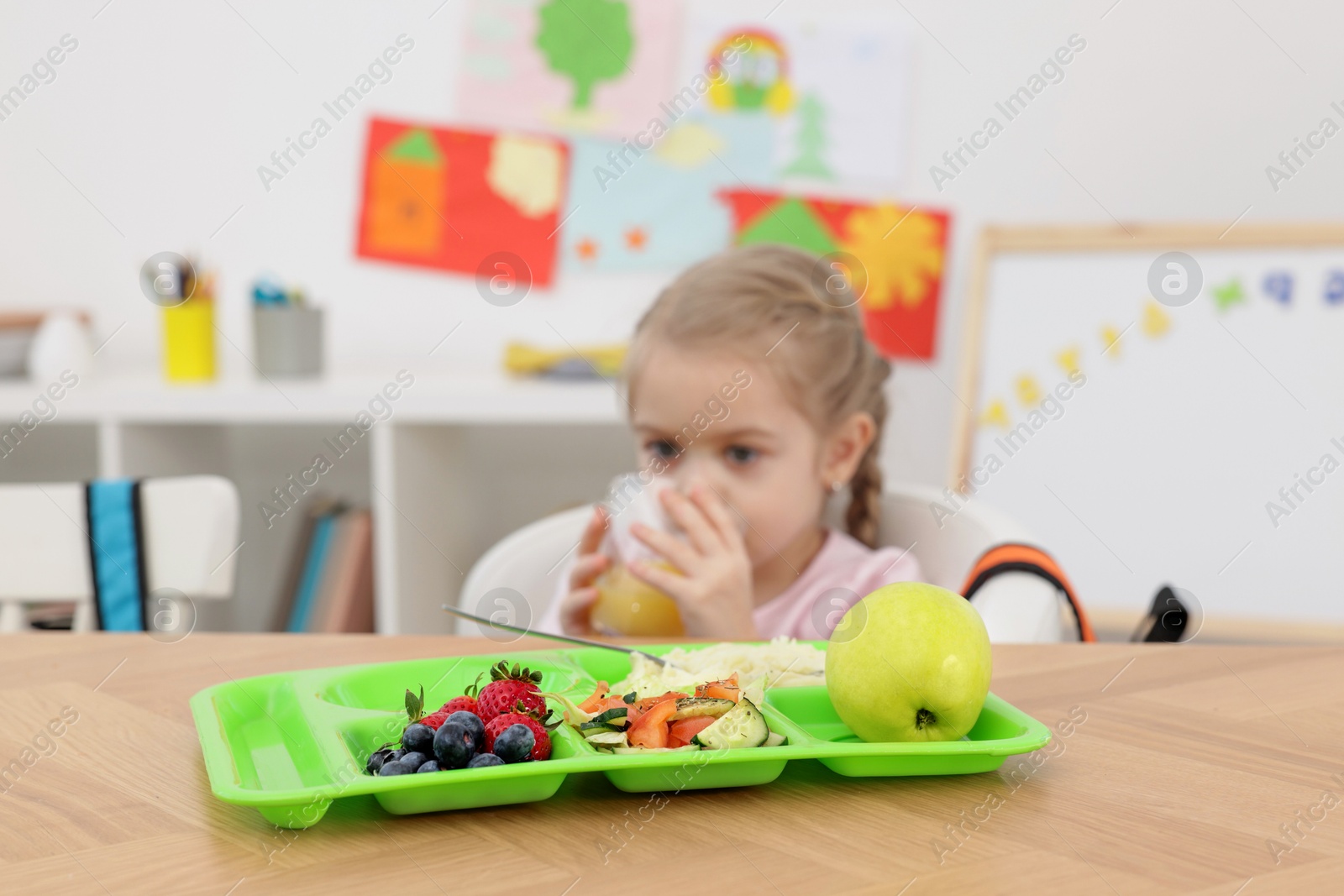 Photo of Cute little girl eating lunch at wooden table in school, selective focus