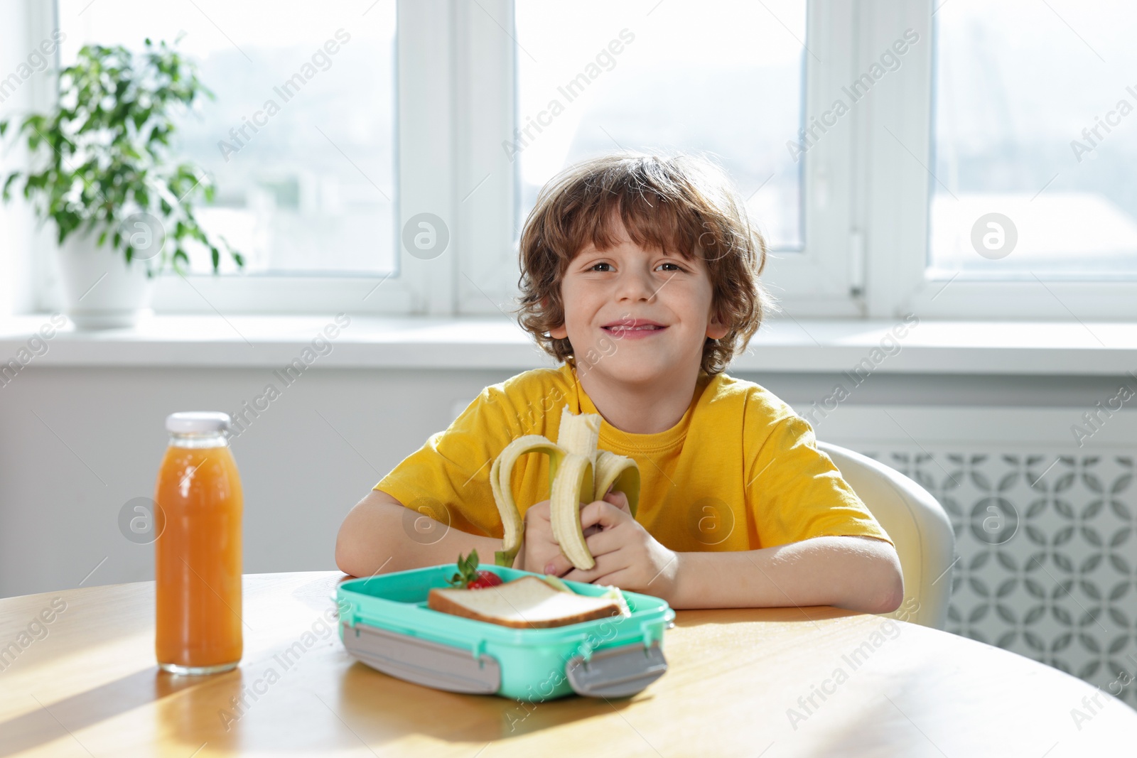 Photo of Cute little boy eating lunch at wooden table in school