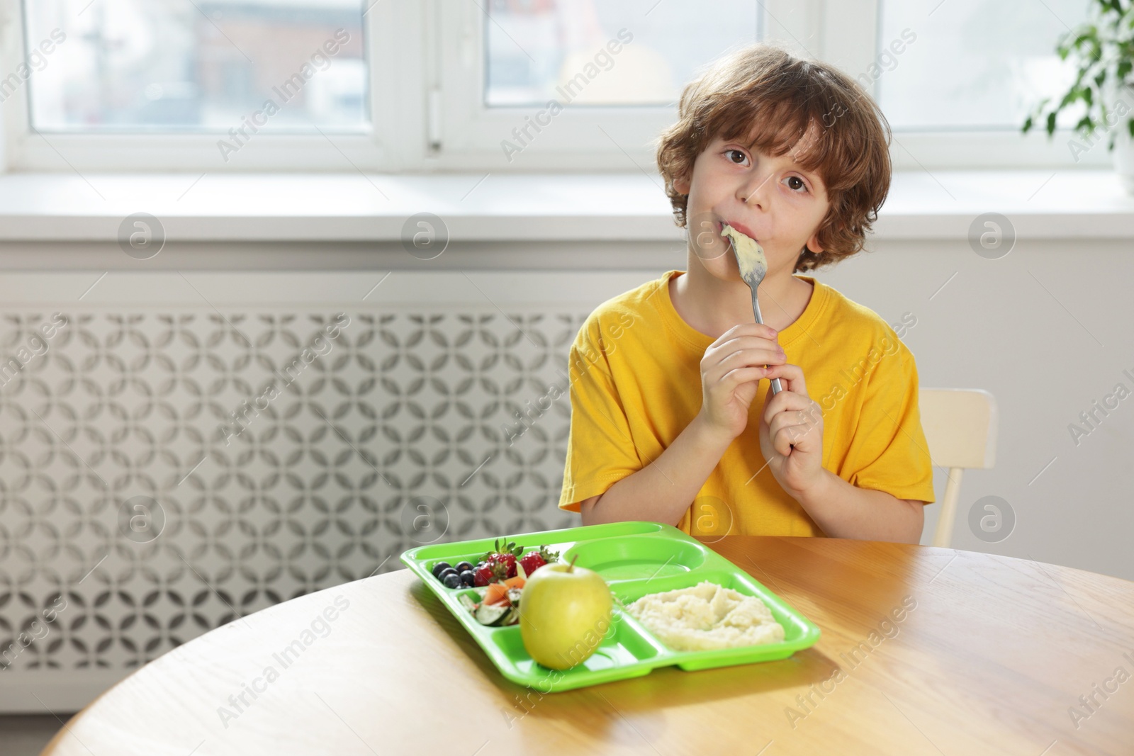 Photo of Cute little boy eating lunch at wooden table in school. Space for text