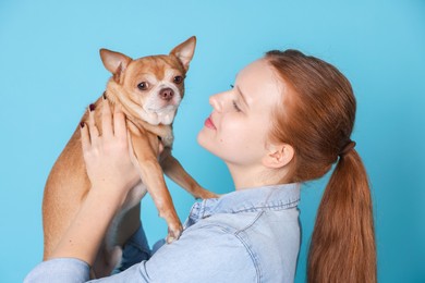 Teenage girl with her cute Chihuahua dog on light blue background