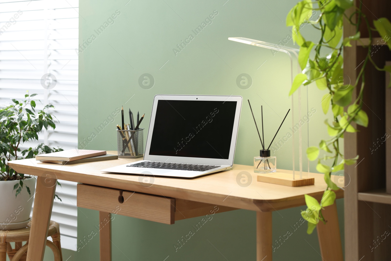 Home office. Comfortable workplace with laptop and stationery on wooden desk in room Photo of Home office. Comfortable workplace with laptop and stationery on wooden desk in room