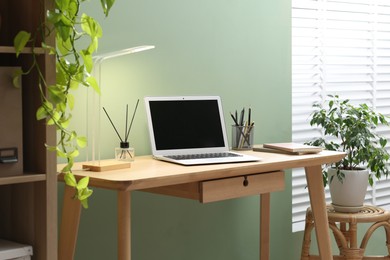 Photo of Home office. Comfortable workplace with laptop and stationery on wooden desk in room