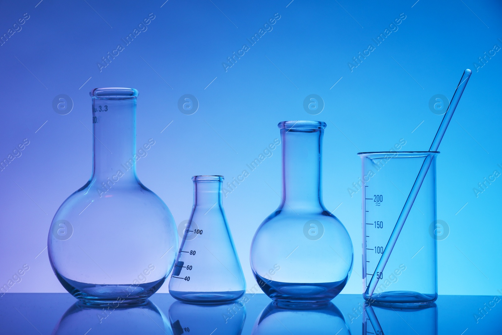 Photo of Laboratory glassware on mirror surface against color background