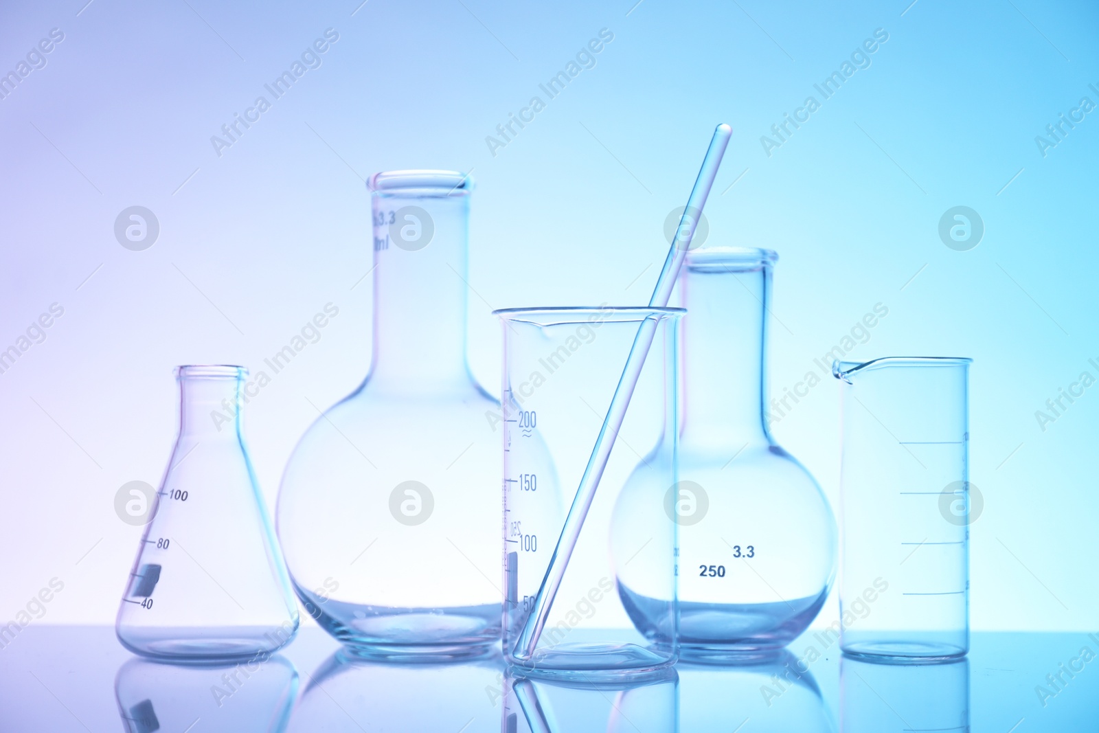 Photo of Laboratory glassware on mirror surface against color background