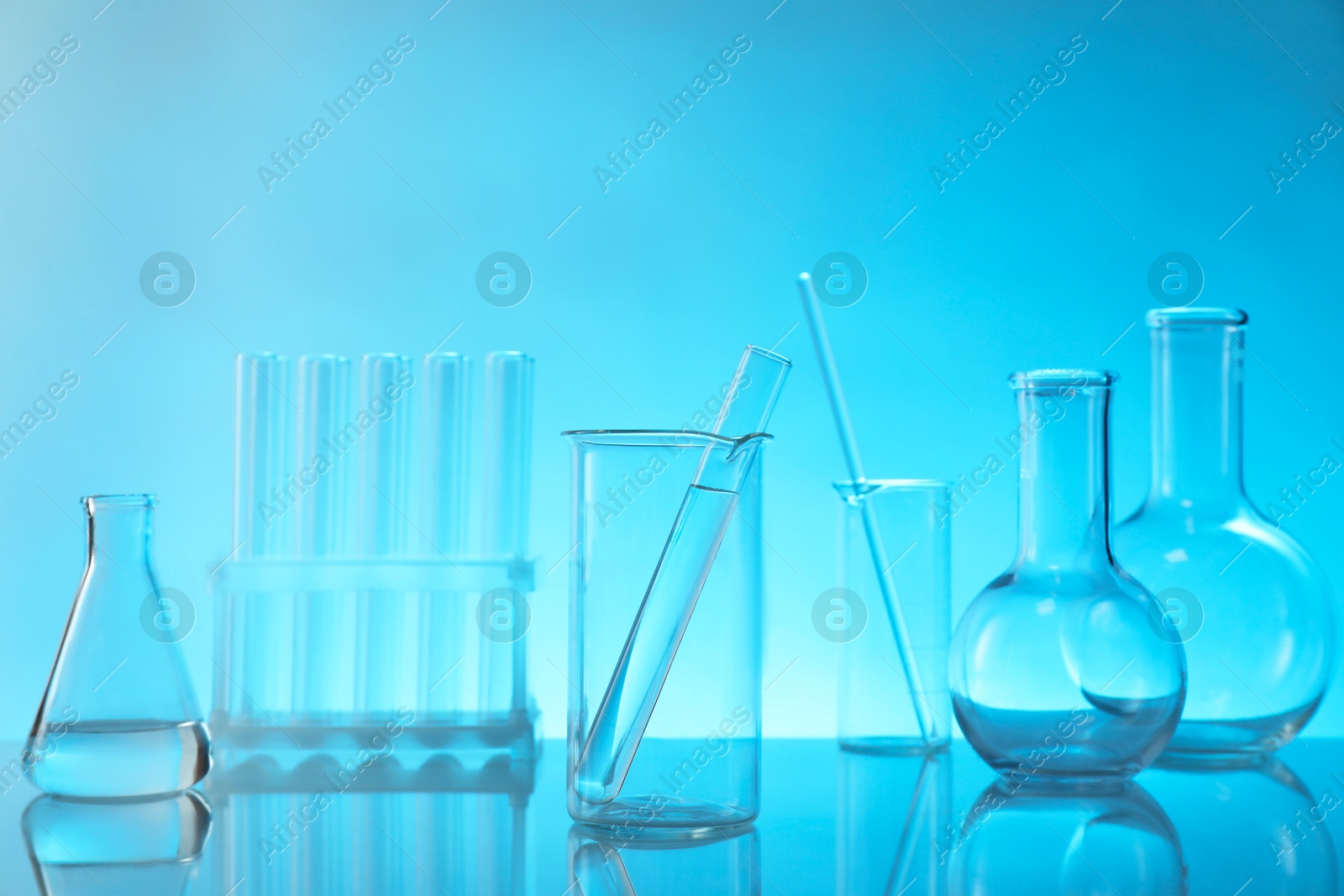 Photo of Laboratory glassware on mirror surface against light blue background