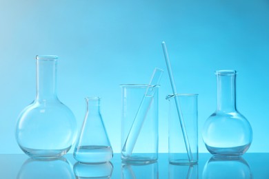 Photo of Laboratory glassware on mirror surface against light blue background