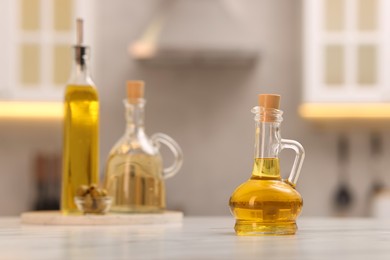 Photo of Bottles of oil on white table in kitchen, space for text