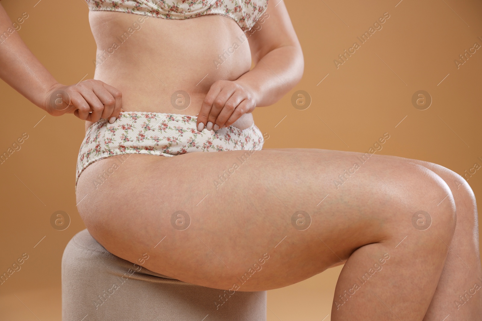 Photo of Woman with cellulite on pouf against dark beige background, closeup