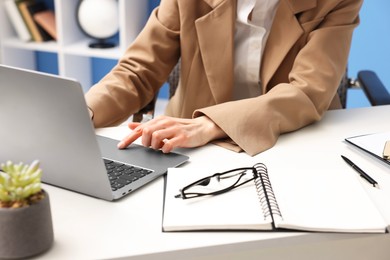 Photo of Secretary working on laptop at table in office, closeup