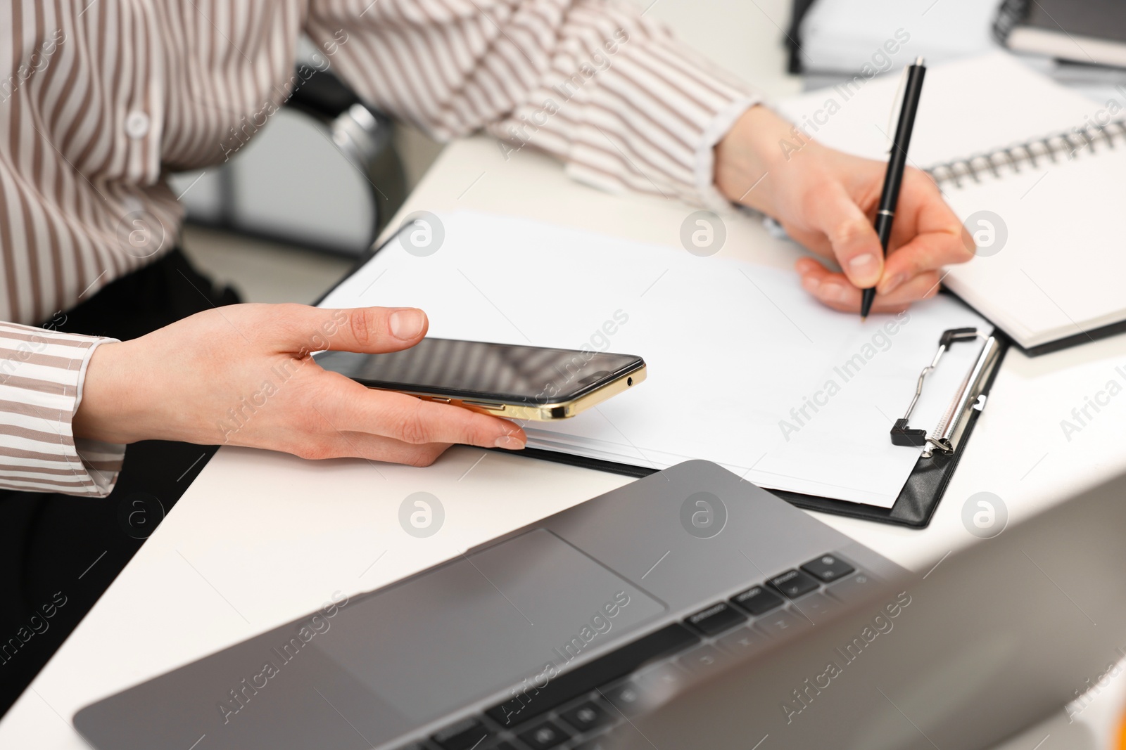 Photo of Secretary with smartphone taking notes at white table in office, closeup