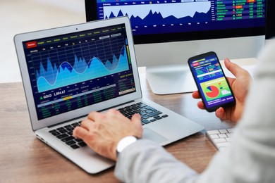 Photo of Financial trading specialist with smartphone and laptop at table in office, closeup