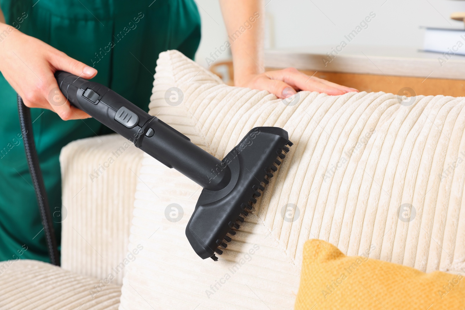 Photo of Professional janitor steam cleaning sofa in room, closeup