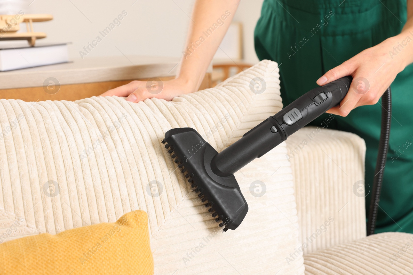 Photo of Professional janitor steam cleaning sofa in room, closeup