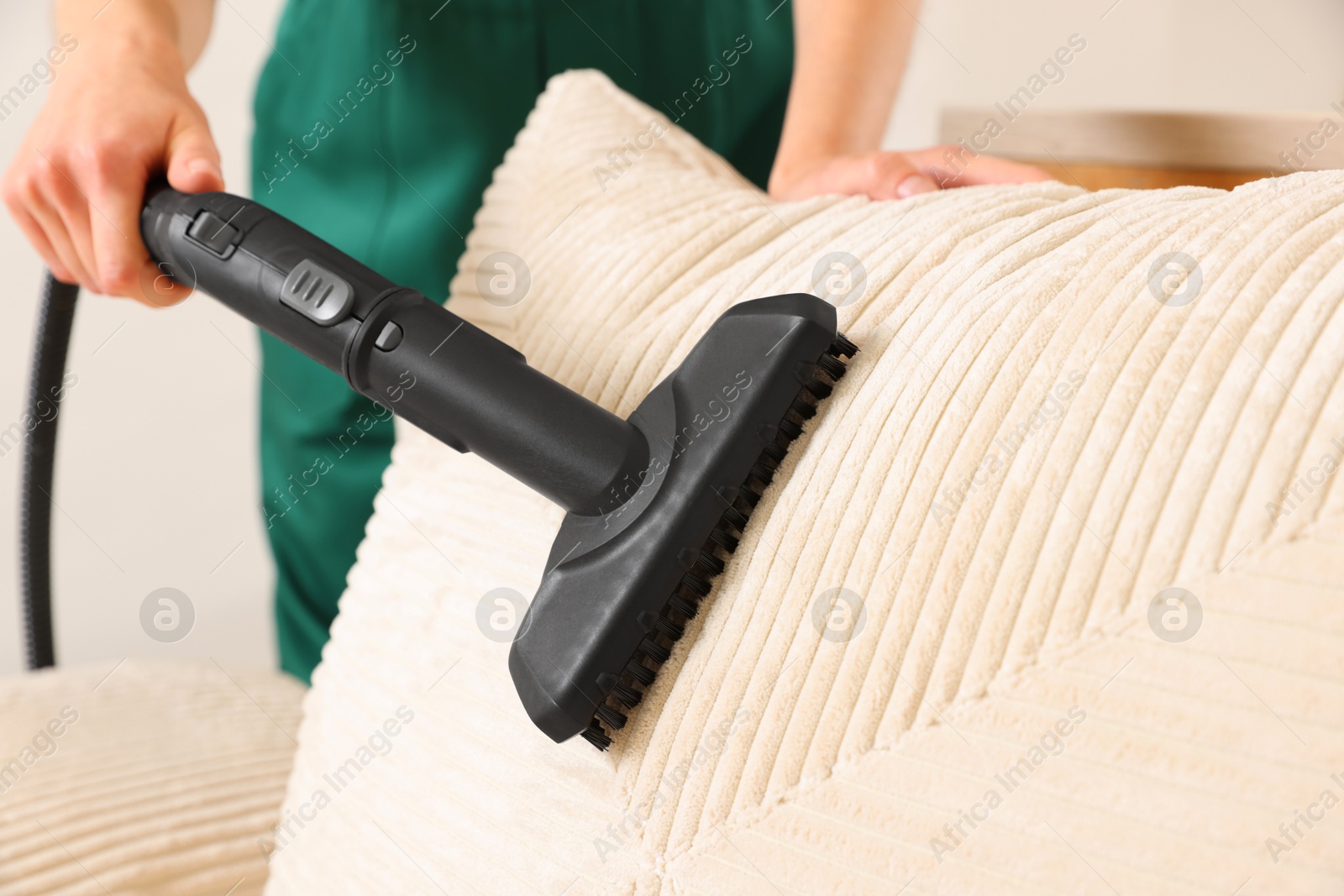 Photo of Professional janitor steam cleaning sofa in room, closeup