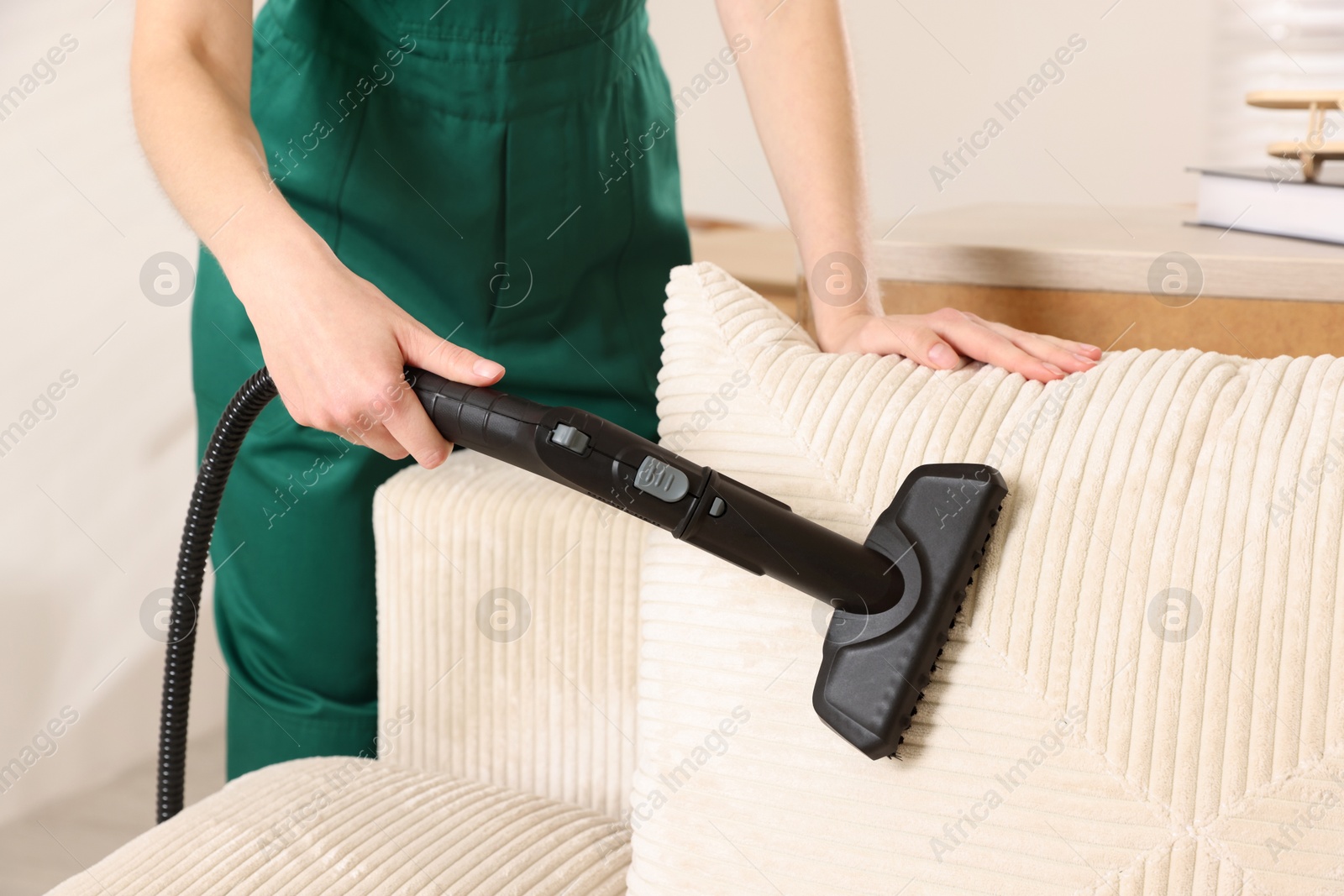 Photo of Professional janitor steam cleaning sofa in room, closeup