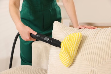 Photo of Professional janitor steam cleaning sofa in room, closeup