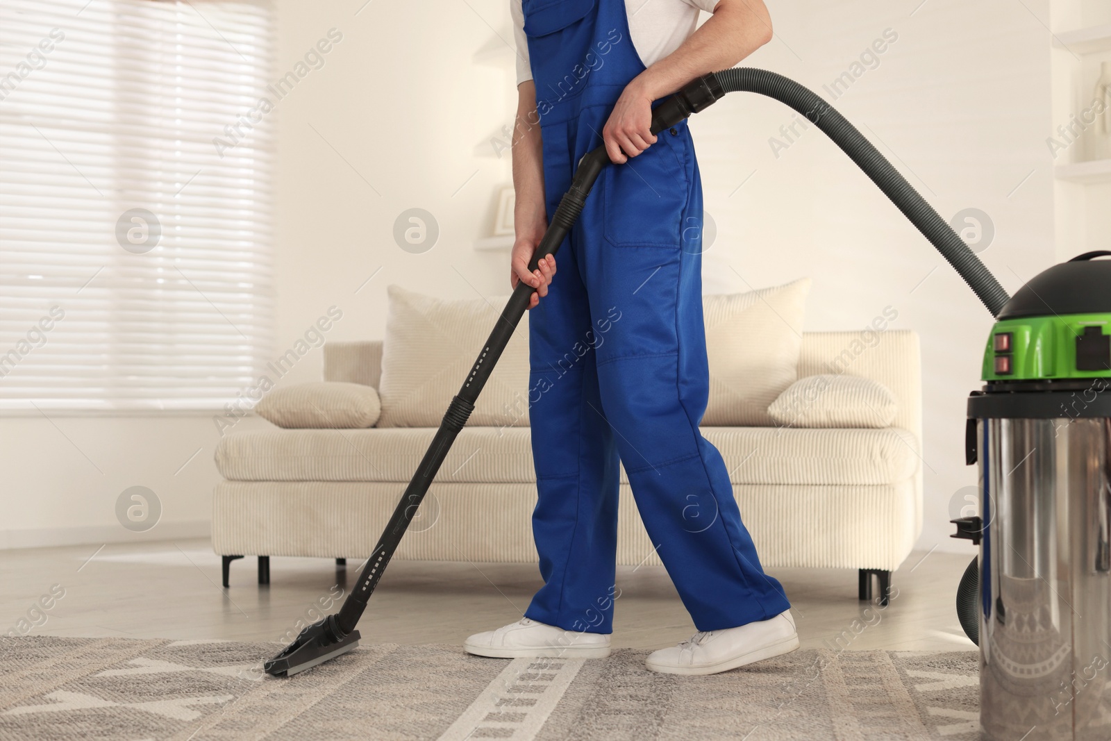 Photo of Cleaning service worker vacuuming rug with professional hoover at home, closeup