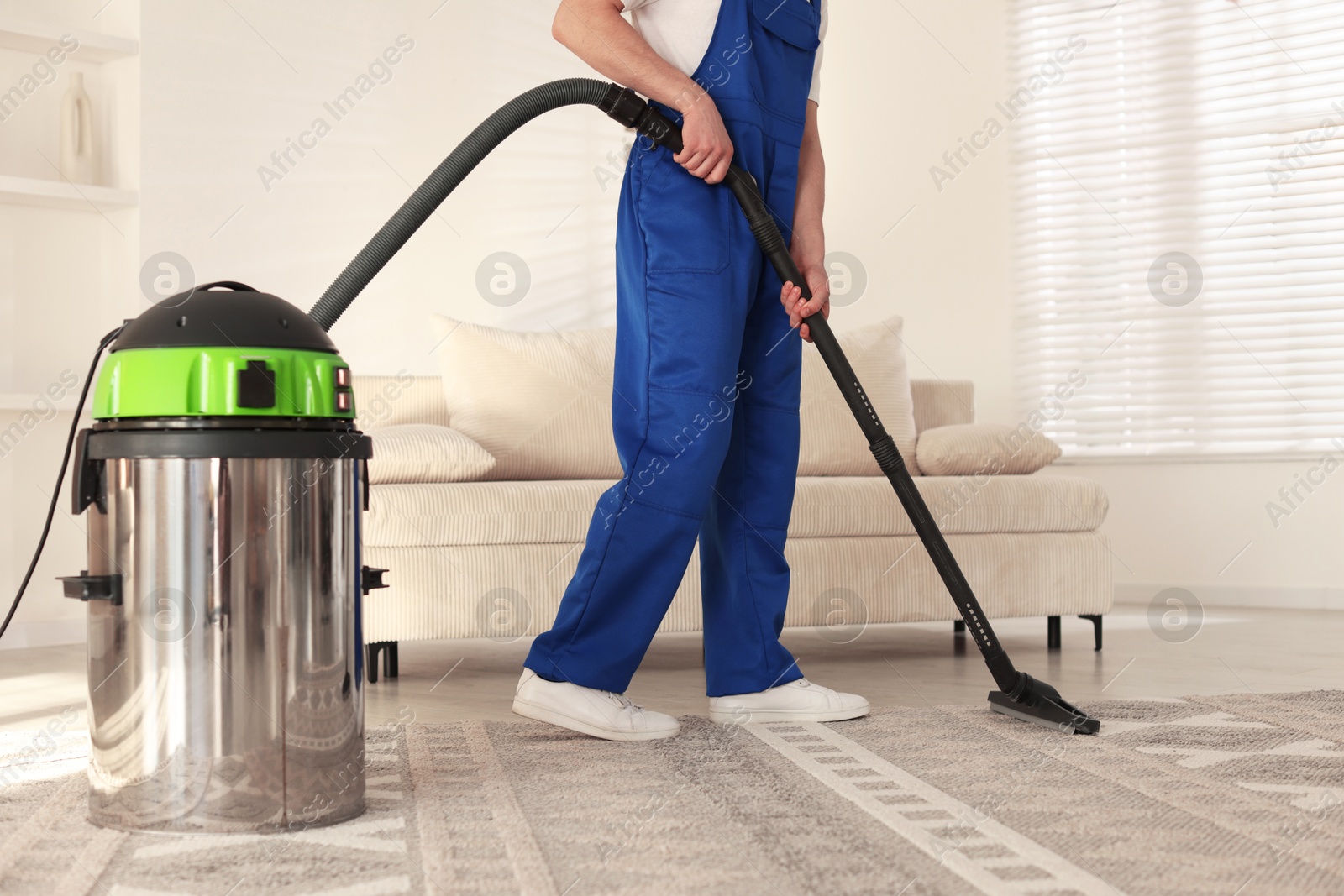 Photo of Cleaning service worker vacuuming rug with professional hoover at home, closeup