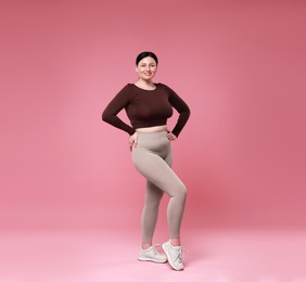 Plus size woman in gym clothes on pink background