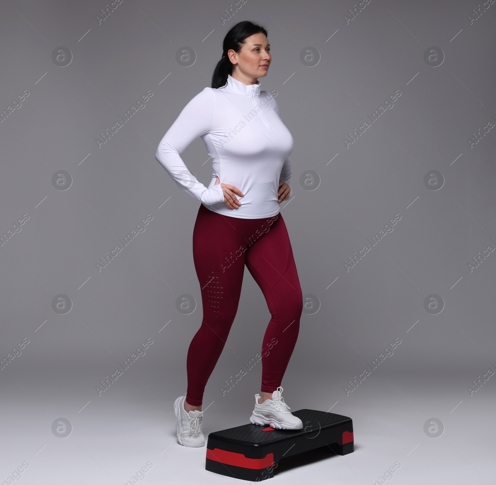 Photo of Plus size woman in gym clothes doing exercise with step platform on grey background