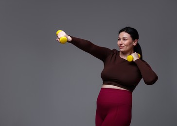 Plus size woman in gym clothes doing exercise with dumbbells on grey background