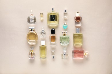 Photo of Bottles of various perfumes on beige background, flat lay