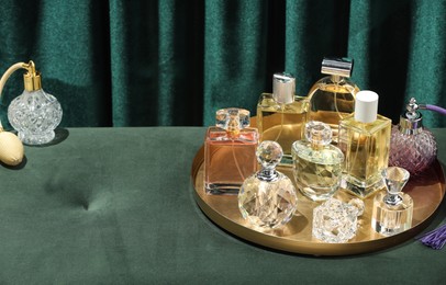 Photo of Different luxury perfumes on green pouf near teal curtains, space for text