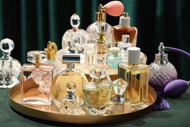 Photo of Different luxury perfumes on green pouf, closeup