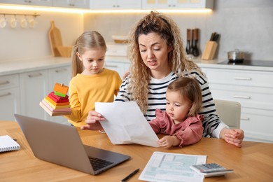 Photo of Work-family balance. Single mother with document and her daughters at table in kitchen