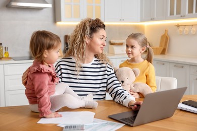 Single mother working on laptop and her daughters at table in kitchen