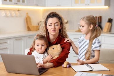 Single mother working with laptop and her daughters at table in kitchen