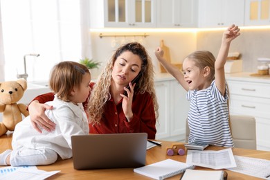 Photo of Work-family balance. Single mother talking on smartphone and her daughters at table in kitchen