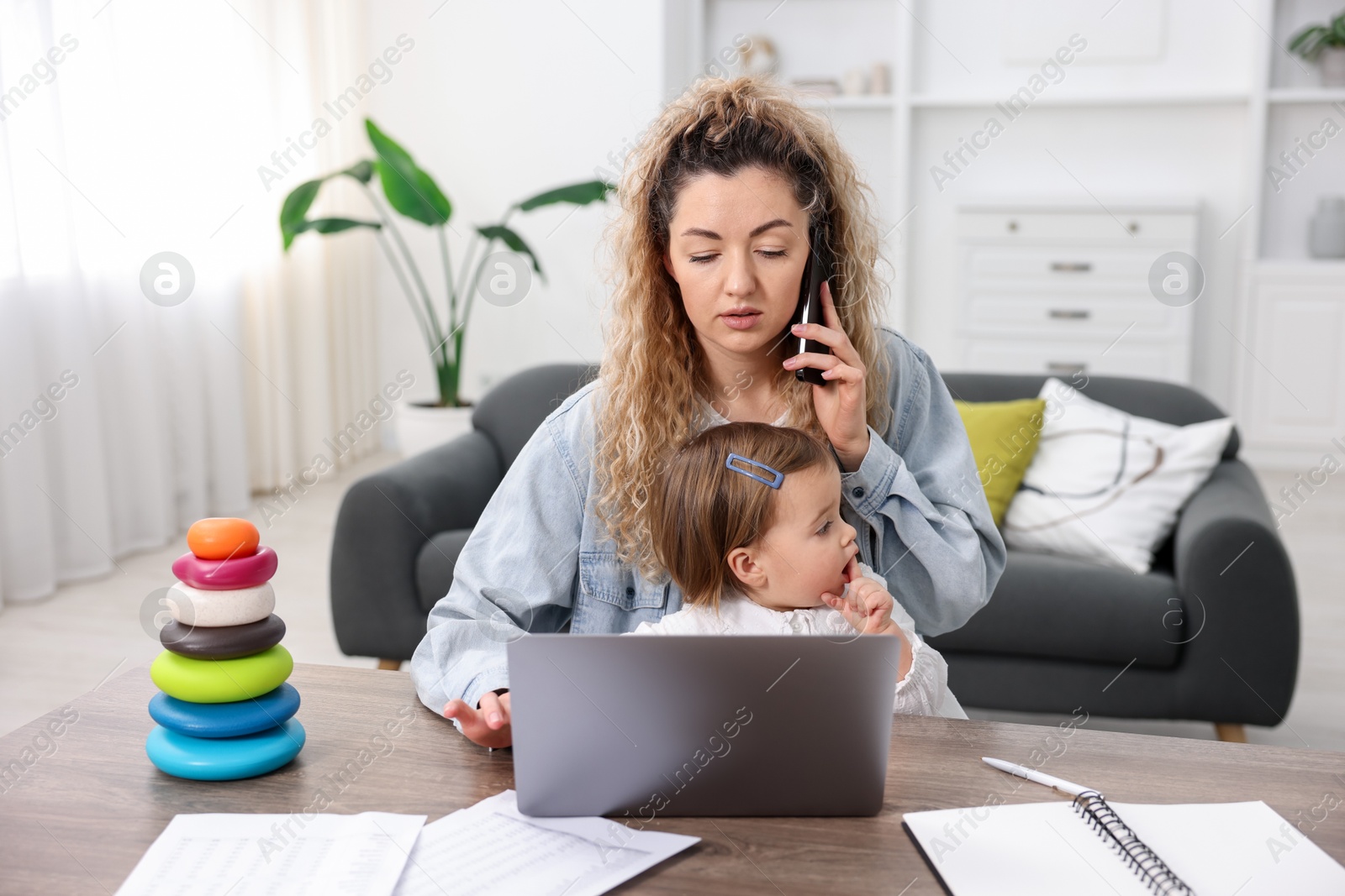 Photo of Work-family balance. Single mother talking on smartphone and her daughter at table indoors