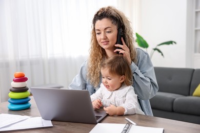 Work-family balance. Single mother talking on smartphone and her daughter at table indoors