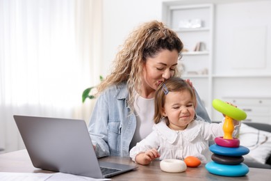 Photo of Single mother kissing her daughter while working at table indoors