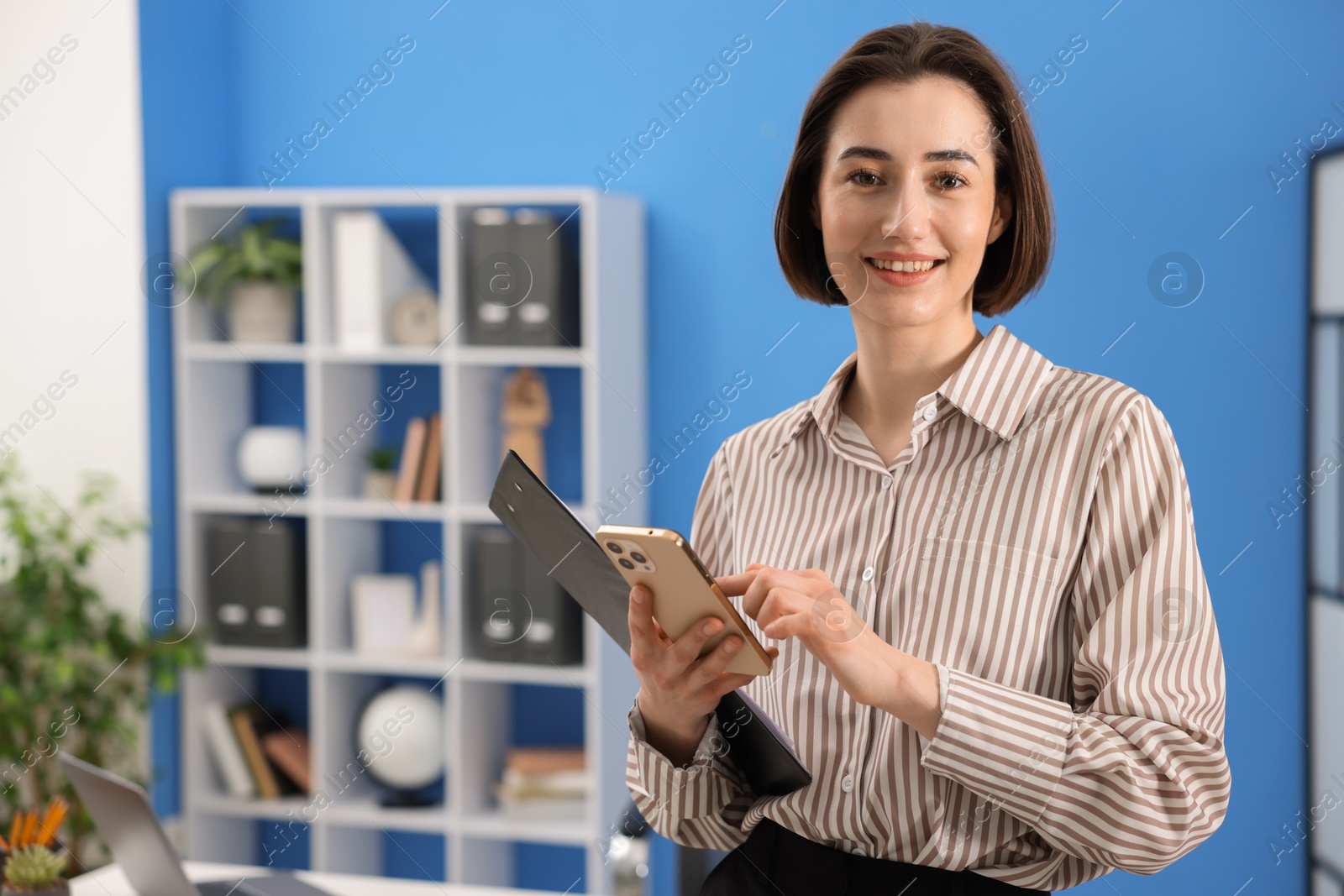 Photo of Smiling secretary with clipboard and smartphone in office. Space for text