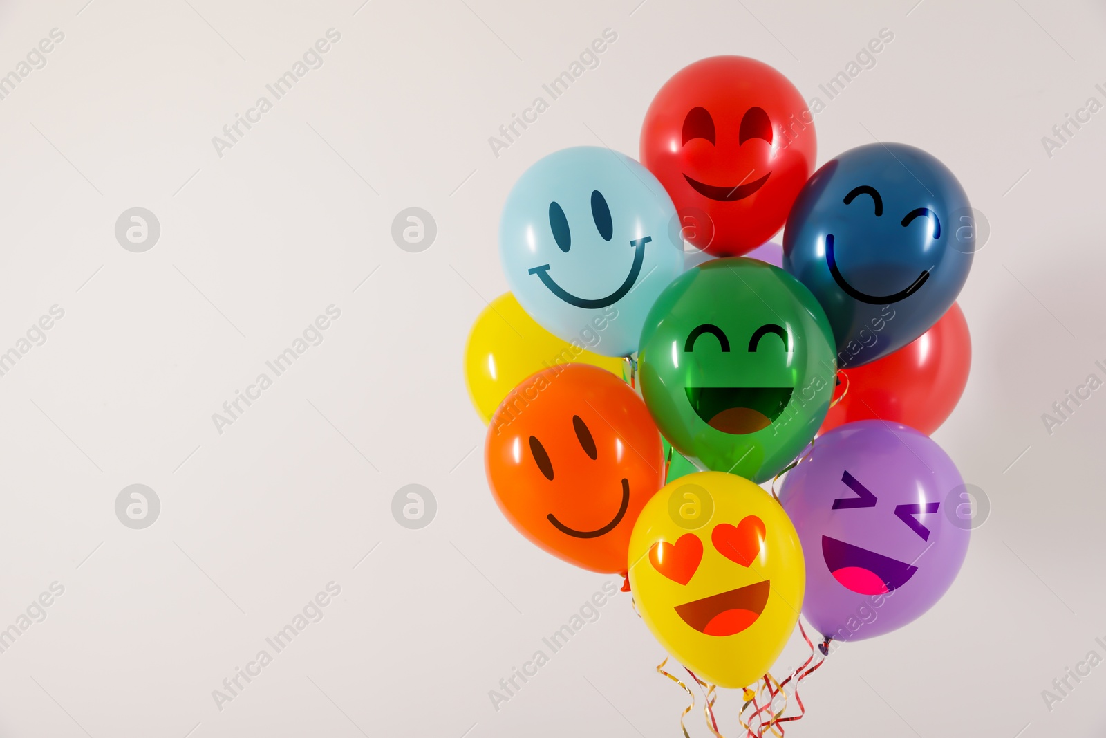 Image of Bright balloons with happy faces on light background, space for text