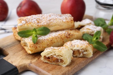 Photo of Tasty apple strudels with powdered sugar and mint on white marble table, closeup