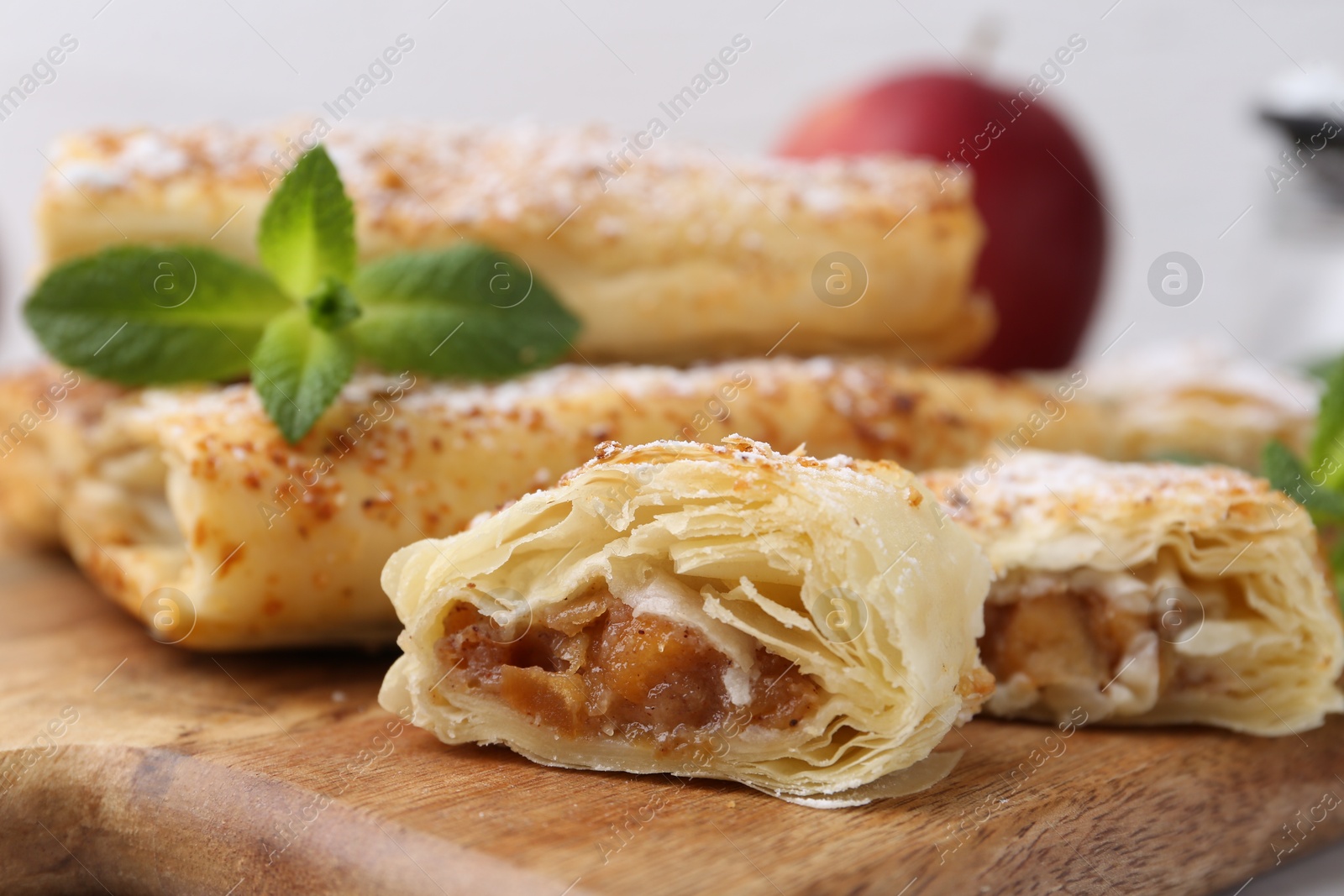 Photo of Tasty apple strudels with powdered sugar and mint on wooden board, closeup