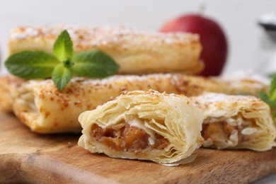 Photo of Tasty apple strudels with powdered sugar and mint on wooden board, closeup