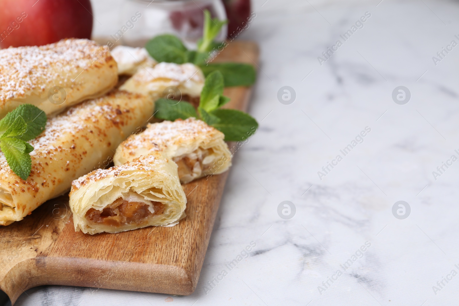 Photo of Tasty apple strudels with powdered sugar and mint on white marble table, closeup. Space for text