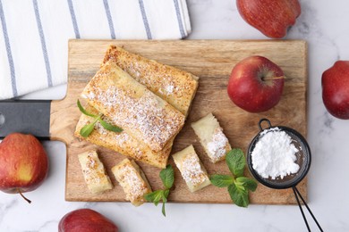 Photo of Tasty apple strudels with powdered sugar, fruits and mint on white marble table, flat lay